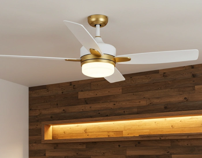 Modern ceiling fan with white blades and a gold base, installed in a room with a wooden accent wall.